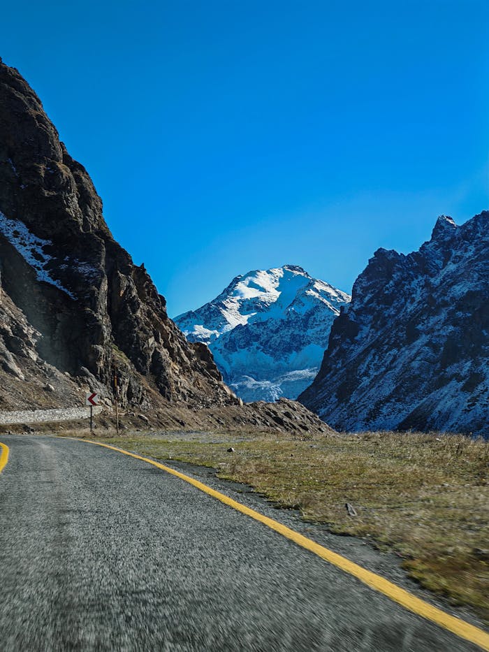 A beautiful mountain road with snow-capped peak under clear blue sky, perfect for travel inspiration.
